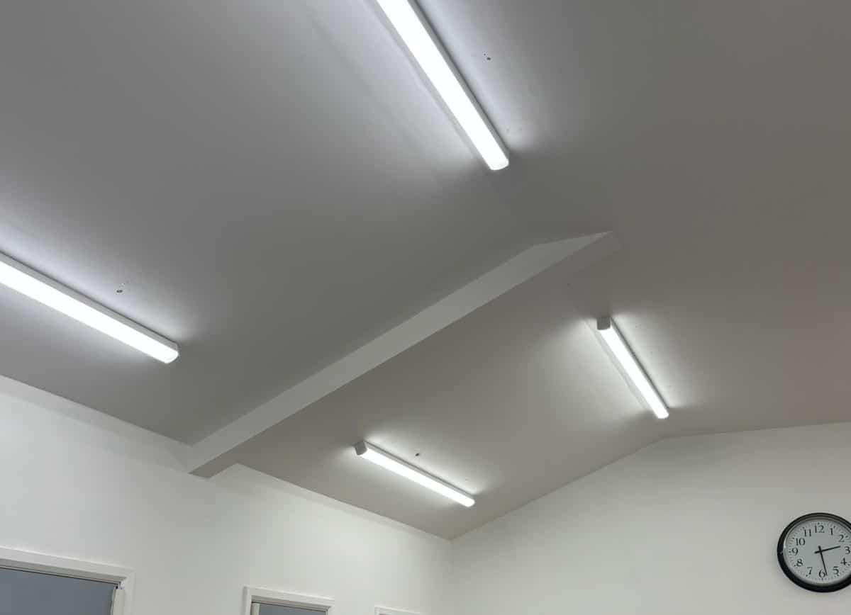 LED tube lights installed on a white ceiling, with a wall clock visible on the right side.